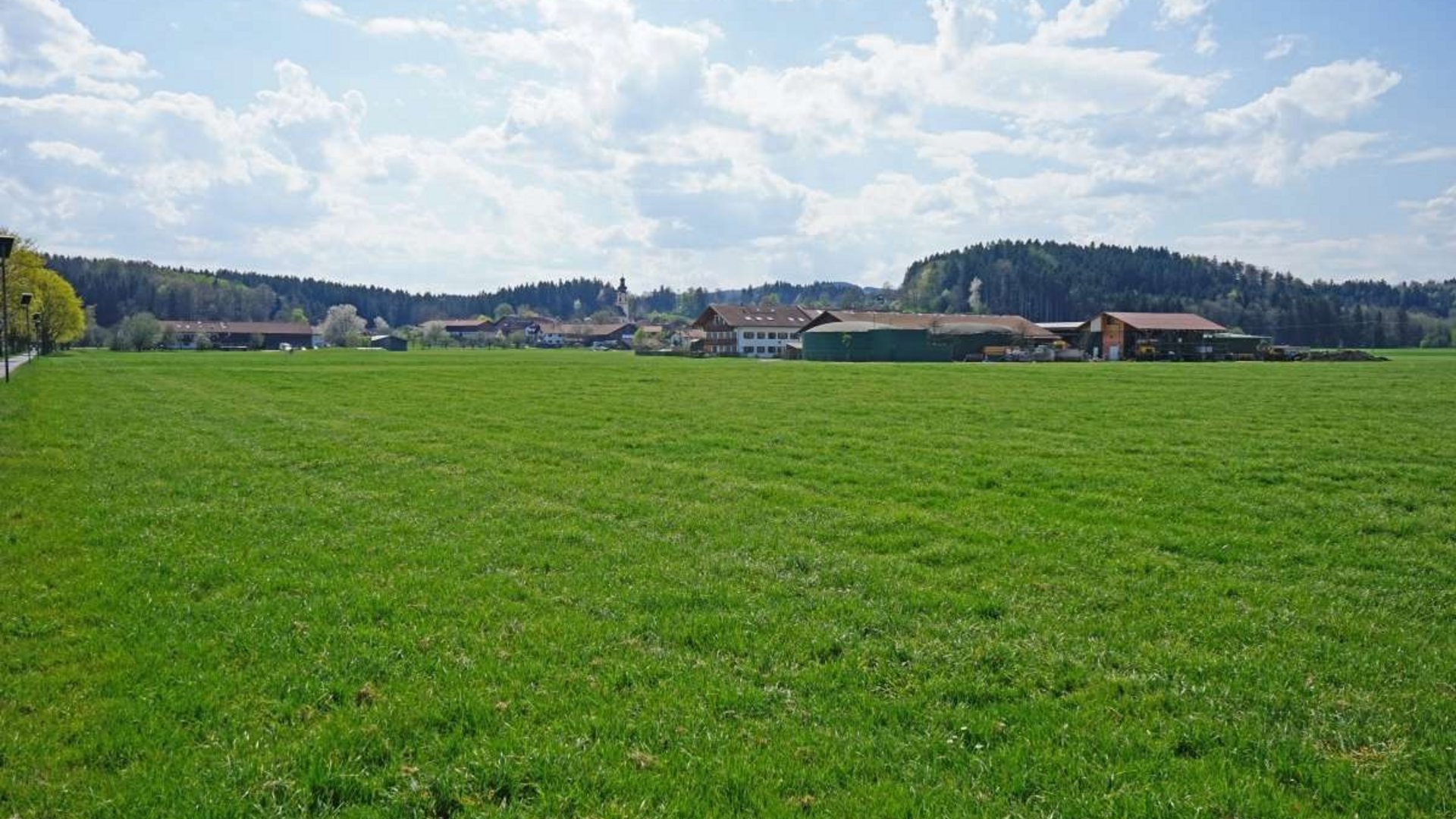 Green field with farm buildings and forest in the background on a cloudy day