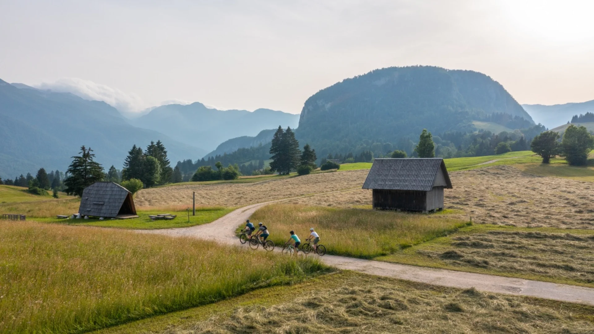 Vier fietsers op een landweg in berglandschap met houten hutten