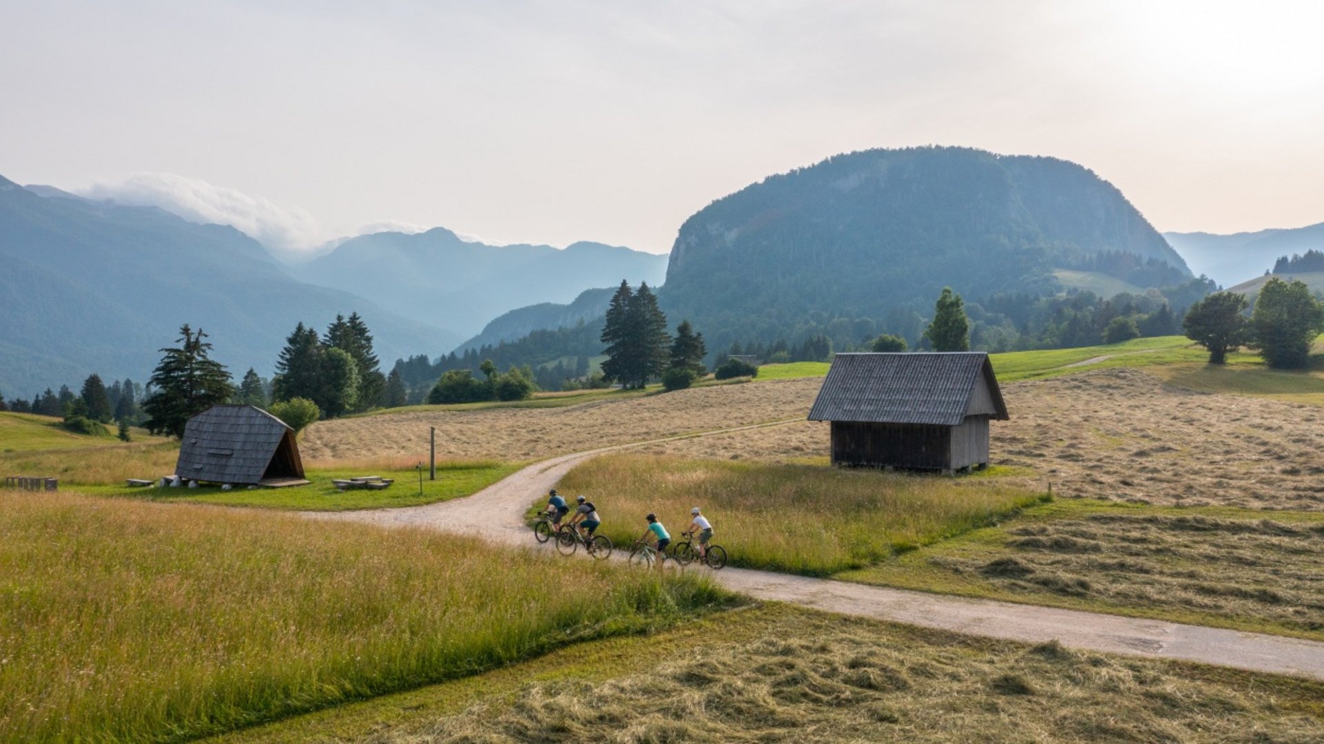 Four cyclists on a dirt path in a mountainous landscape with wooden huts
