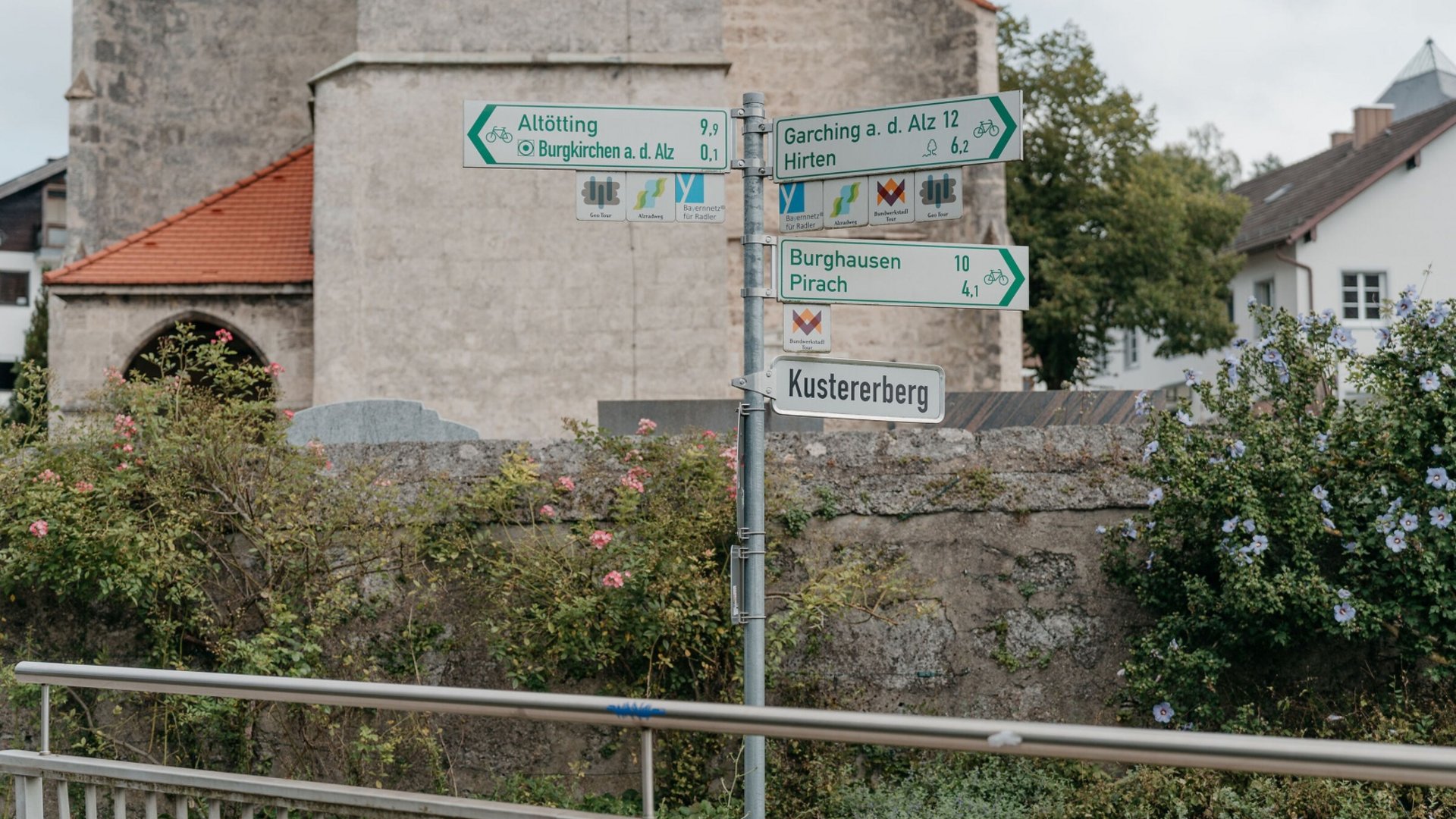 Signpost showing distances to German towns and bike routes near a building