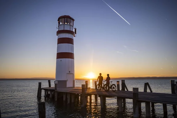 Burgenland © Heiko Mandl Leuchtturm am Pier bei Sonnenuntergang mit zwei Personen und Fahrrädern