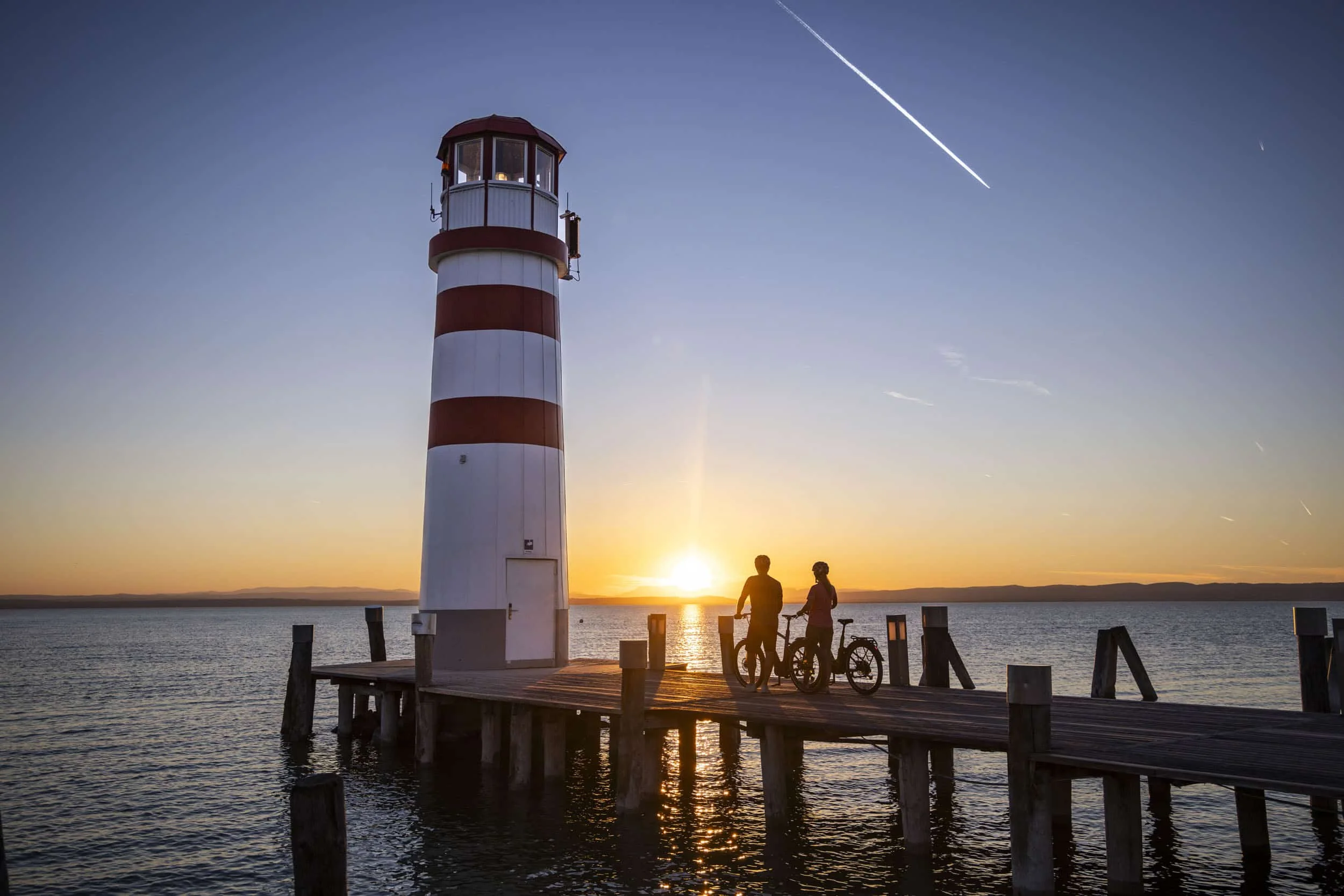 Burgenland © Heiko Mandl Leuchtturm am Pier bei Sonnenuntergang mit zwei Personen und Fahrrädern