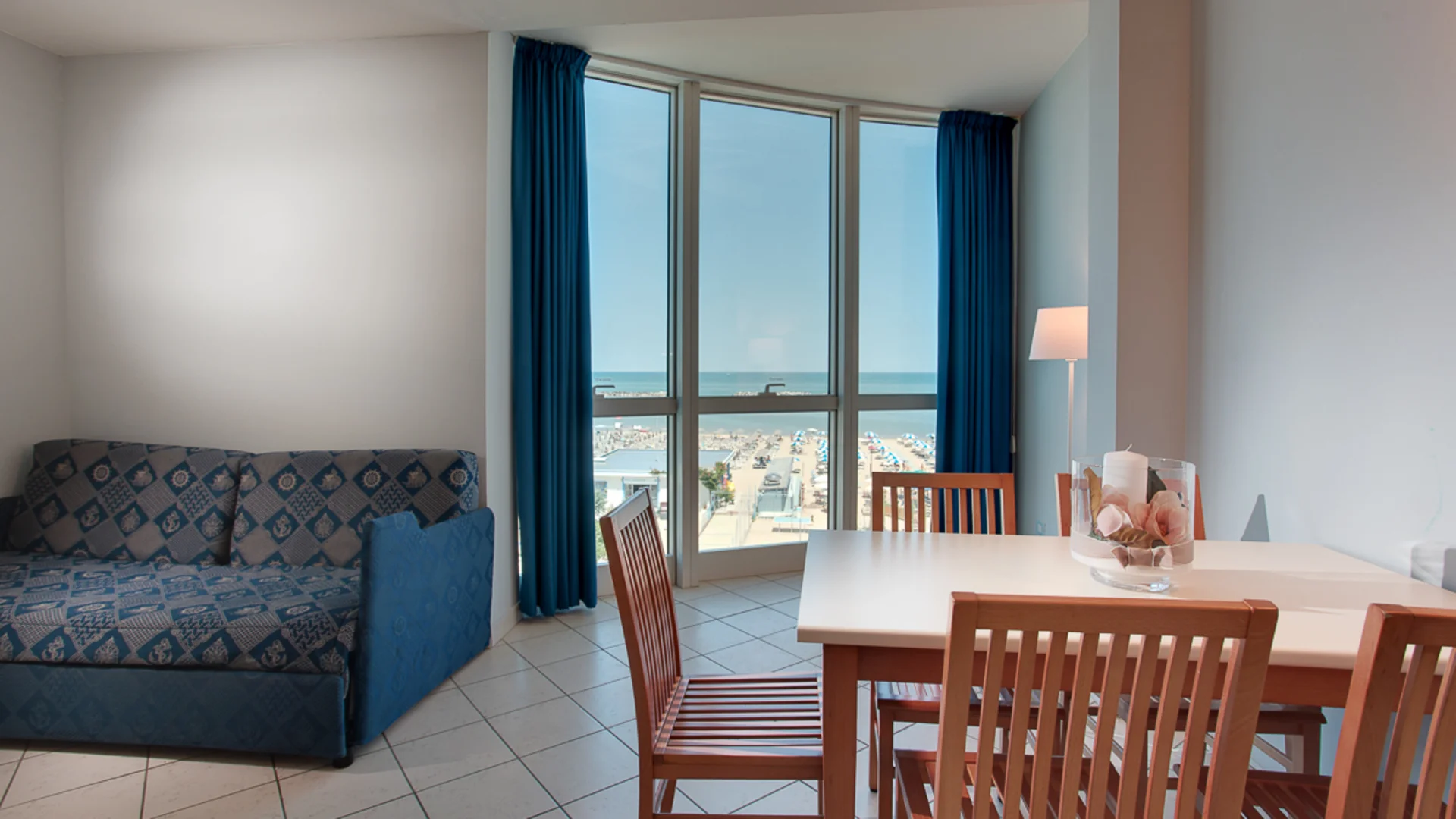 Living room with blue sofa, wooden table and chairs overlooking the sea