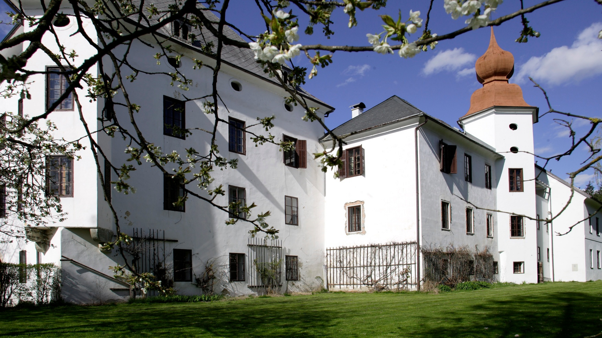 White castle with orange tower top and blooming tree in front