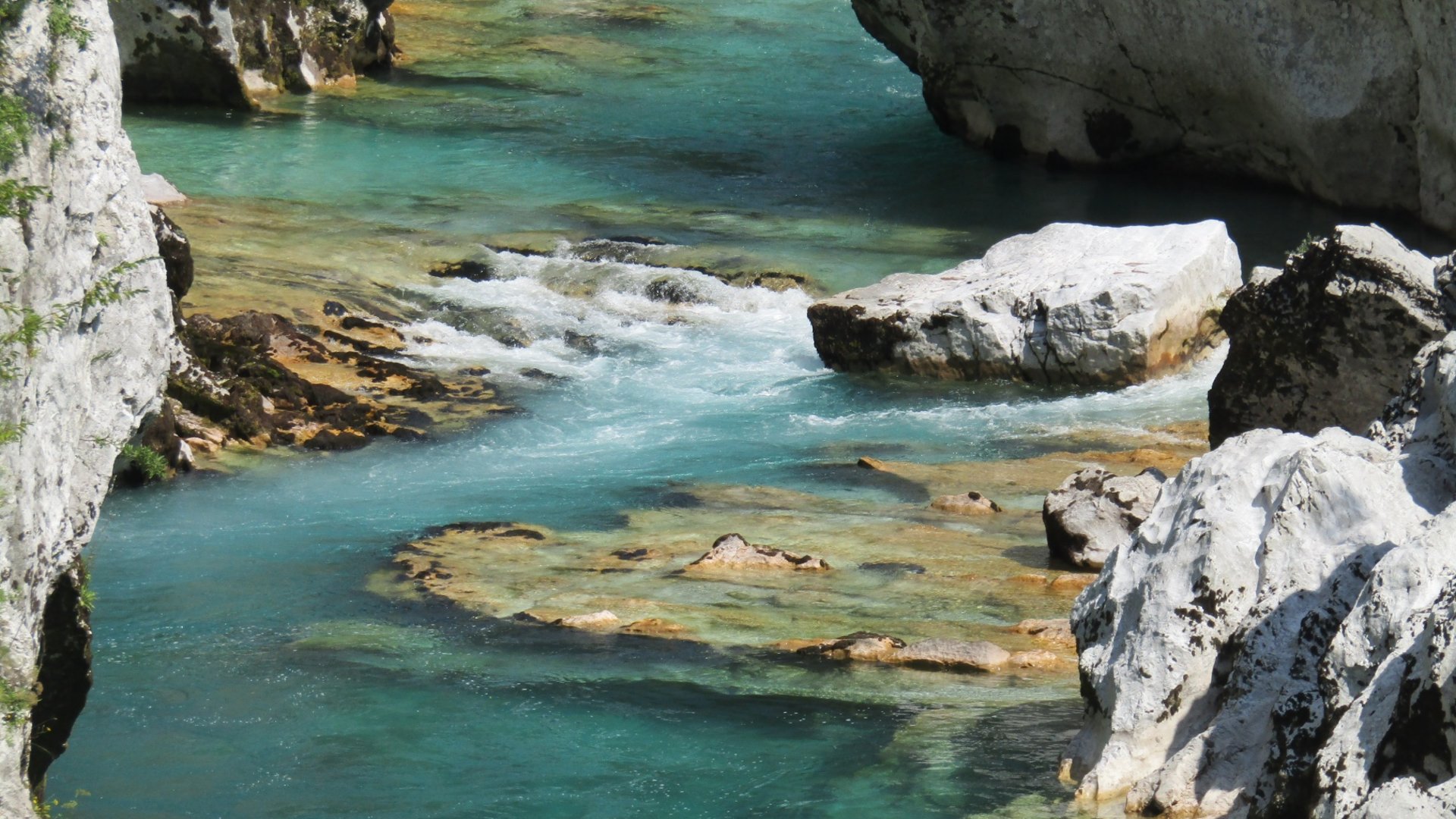 Clear blue water flowing between large rocks in a mountain gorge