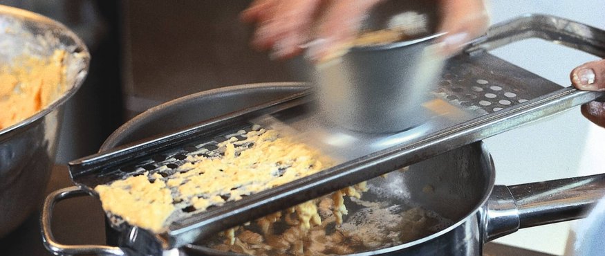 Person reibt Lebensmittel über eine Reibe in einen Kochtopf