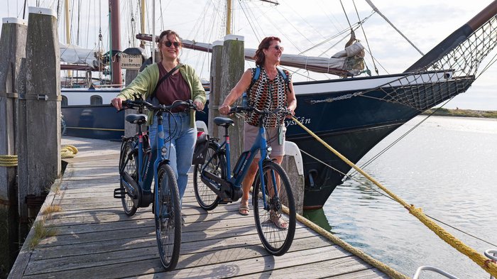 Boat Bike Tours © Boat Bike Tours Zwei Frauen mit Fahrrädern auf einem Holzsteg neben einem Segelboot