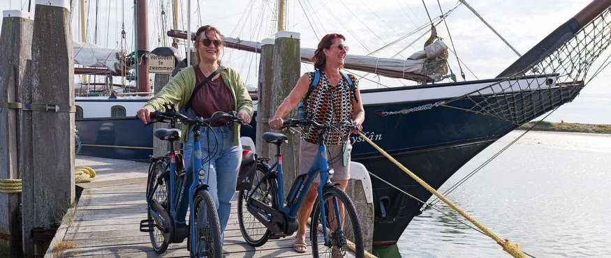 Zwei Frauen mit Fahrrädern auf einem Holzsteg neben einem Segelboot