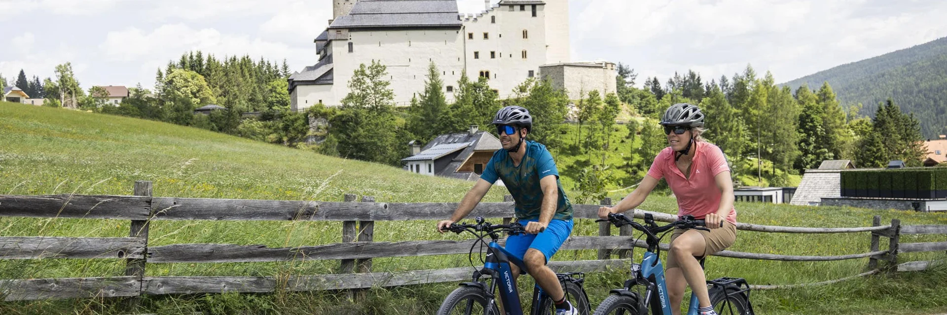 Twee fietsers rijden op landweg met kasteel en groene weide op de achtergrond