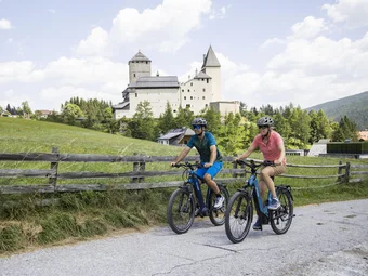 Salzburg Lungau © Velontour - Heiko Mandl Two cyclists riding on country road with castle and green meadow in background