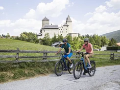 Twee fietsers rijden op landweg met kasteel en groene weide op de achtergrond