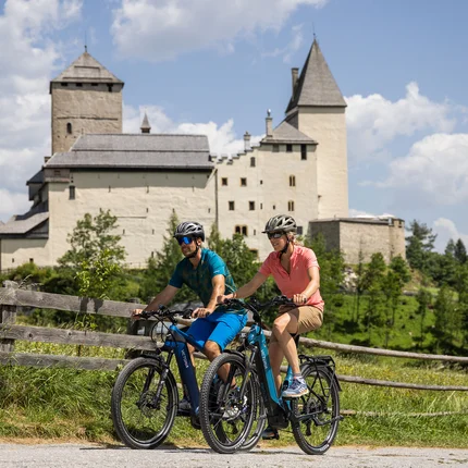 Zwei Radfahrer vor einer historischen Burg bei sonnigem Wetter