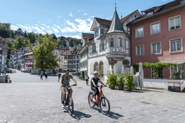 Switzerland Two people riding bikes on a sunny day through an old town square