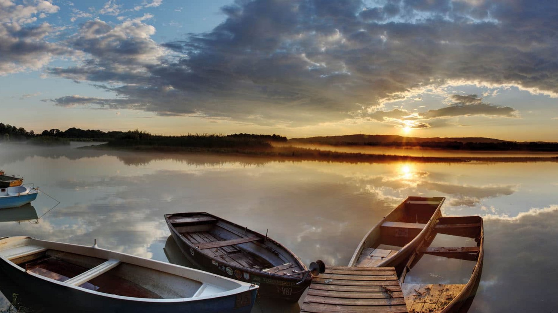 Boats on calm lake at sunrise with reflective water surface