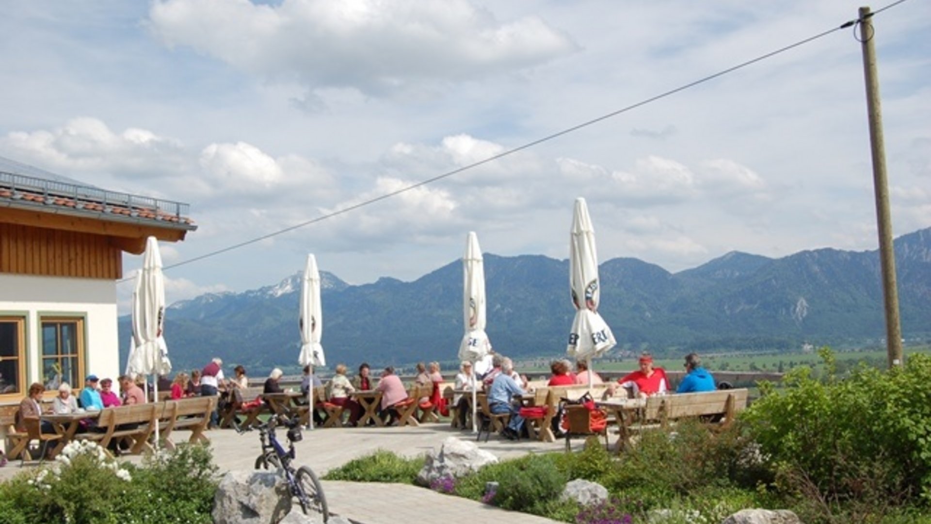 People sitting outside on wooden benches in mountain landscape with umbrellas