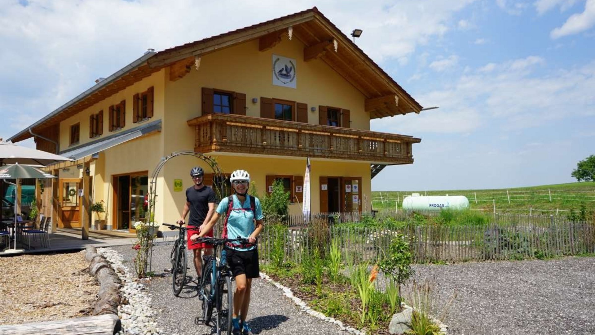 Two cyclists walking their bikes in front of a yellow country house