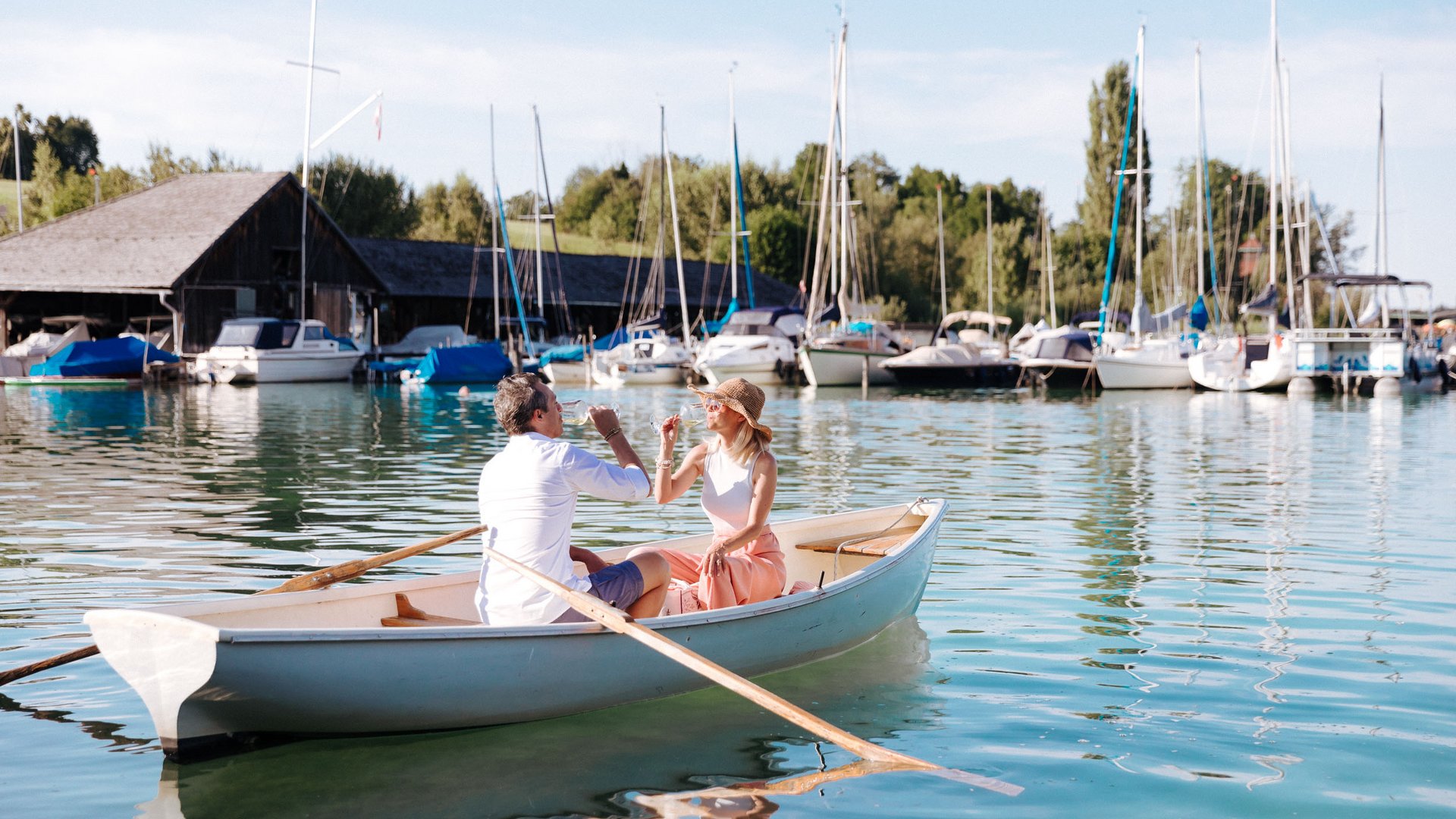 Couple drinking prosecco in rowboat at sunny marina