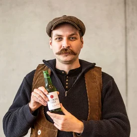 Man met snor houdt fles pilsbier vast in traditionele kleding