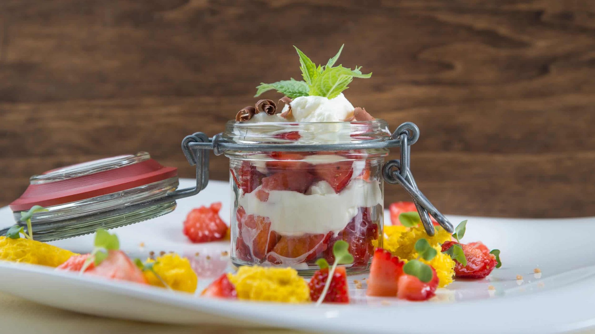 Dessert in a jar with berries, cream, and mint leaf on a white plate
