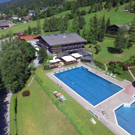 Outdoor pool with water slide next to hotel in green mountain landscape