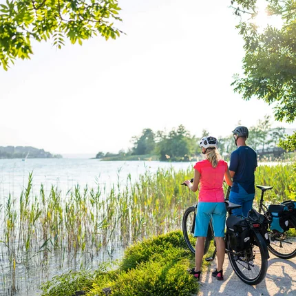 Stel met fietsen kijkt naar zonnig meer aan weelderige oever