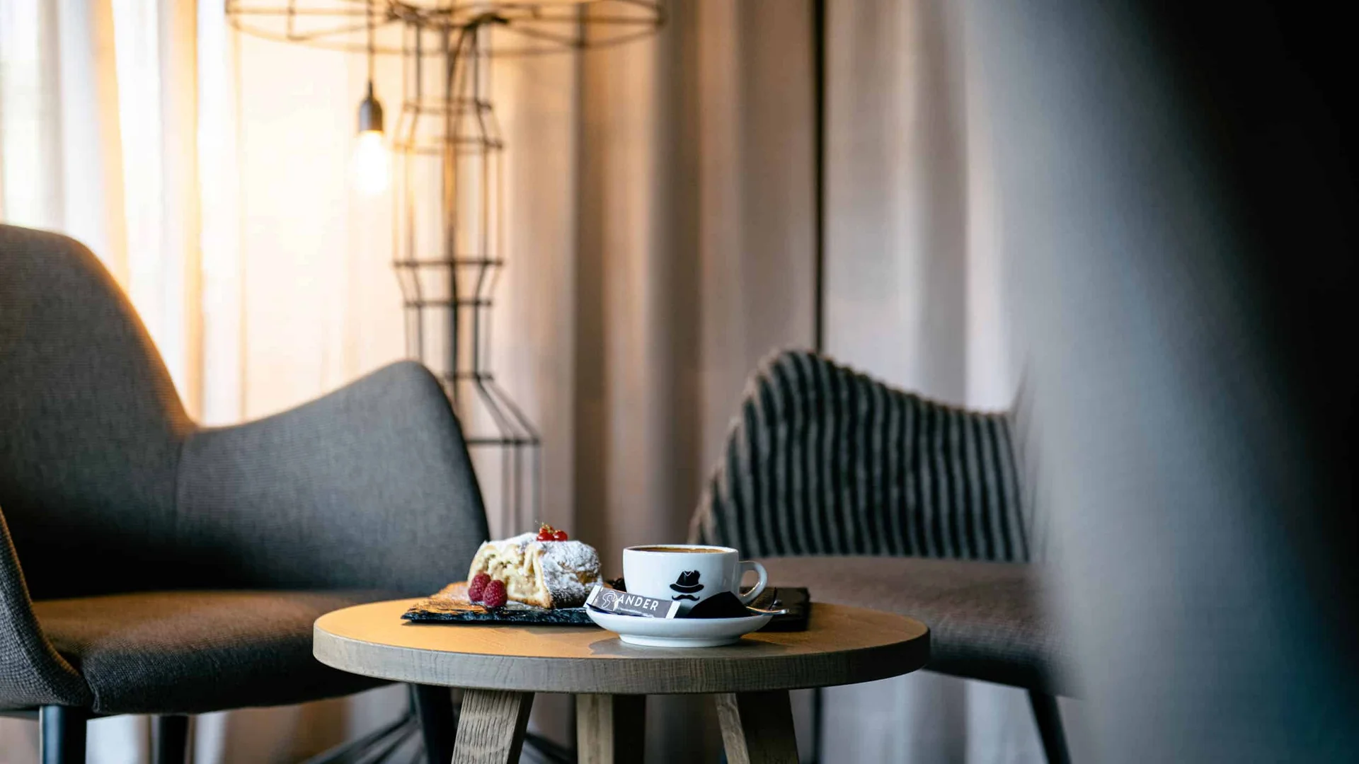 Cup of coffee and cake on wooden table between chairs in cozy room