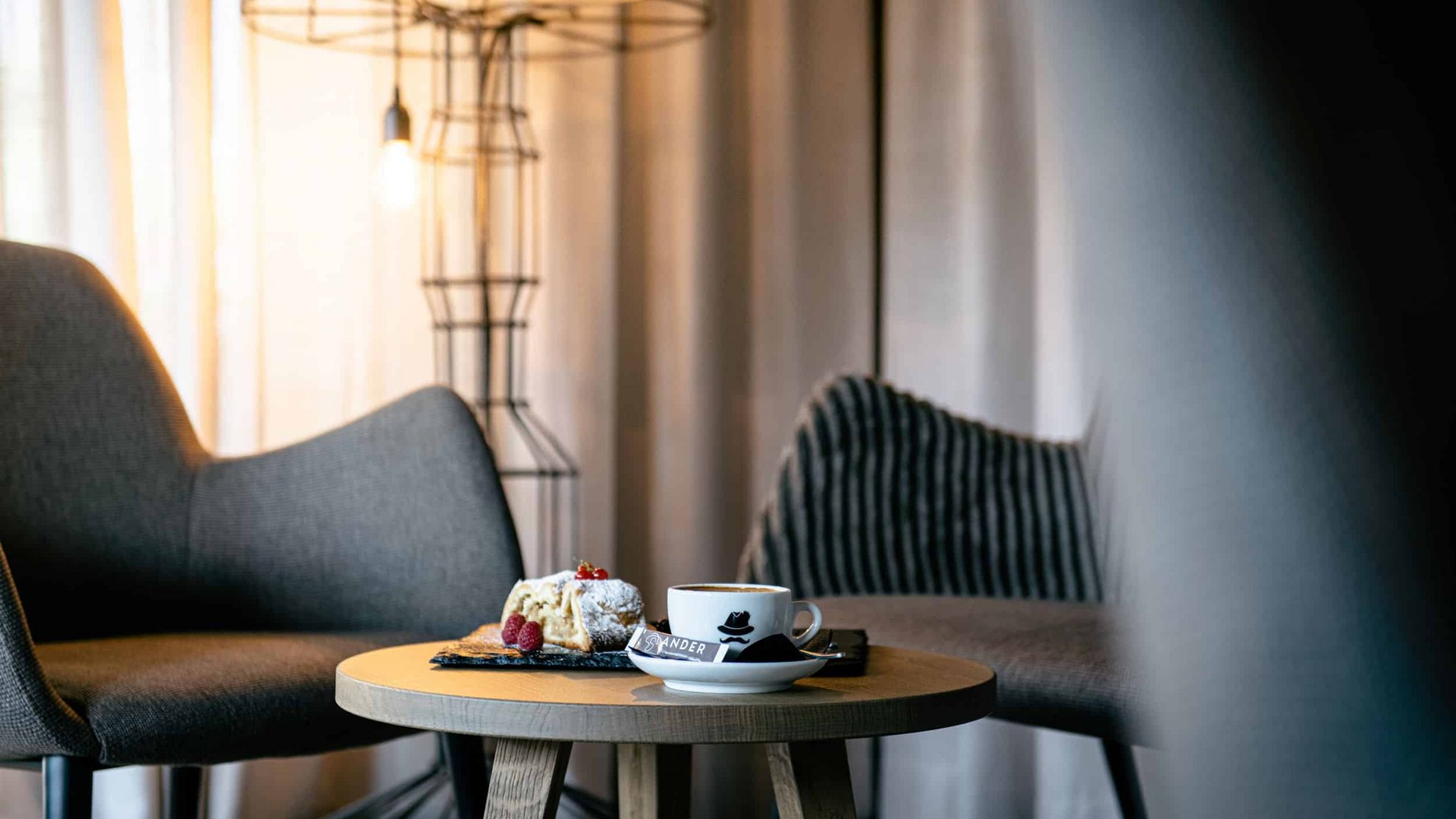 Cup of coffee and cake on wooden table between chairs in cozy room