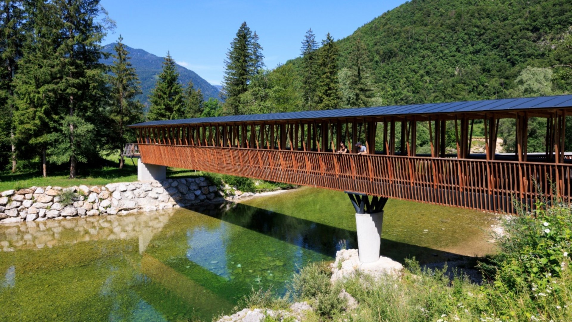 Covered wooden bridge over clear river in mountainous landscape