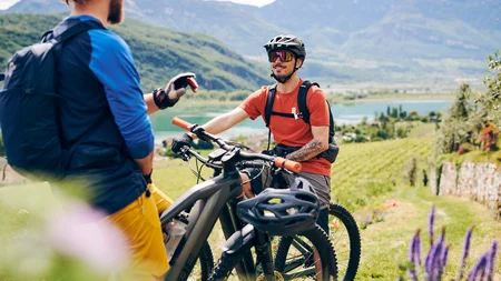 Kulinarisch unterwegs in Tramin © IDM Südtirol - Manuel Ferrigato Zwei Männer mit Mountainbikes in bergiger Landschaft sprechen miteinander