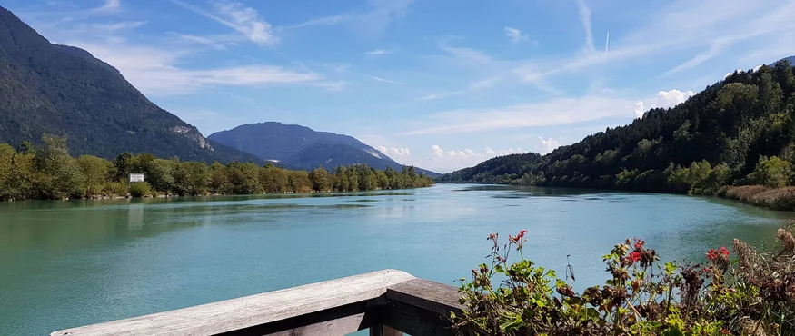 Rivier met bergen, blauwe lucht en houten railing met bloemen op de voorgrond