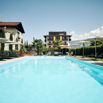 View of an outdoor pool with loungers and umbrellas in front of a building