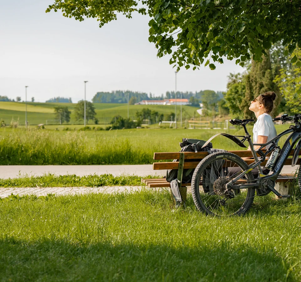 3 Gründe fürs Herbst-Radln in Inn-Salzach © Tourismusverein Inn-Salzach Frau auf Parkbank neben Fahrrad genießt sonnige Landschaft