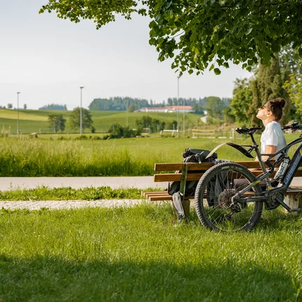 3 Gründe fürs Herbst-Radln in Inn-Salzach © Tourismusverein Inn-Salzach Frau auf Parkbank neben Fahrrad genießt sonnige Landschaft
