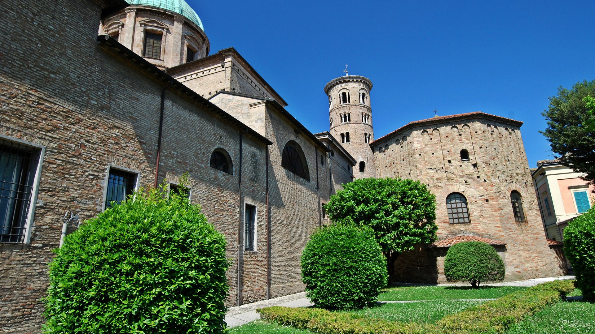 Historic church with round tower and well-kept garden under clear blue sky