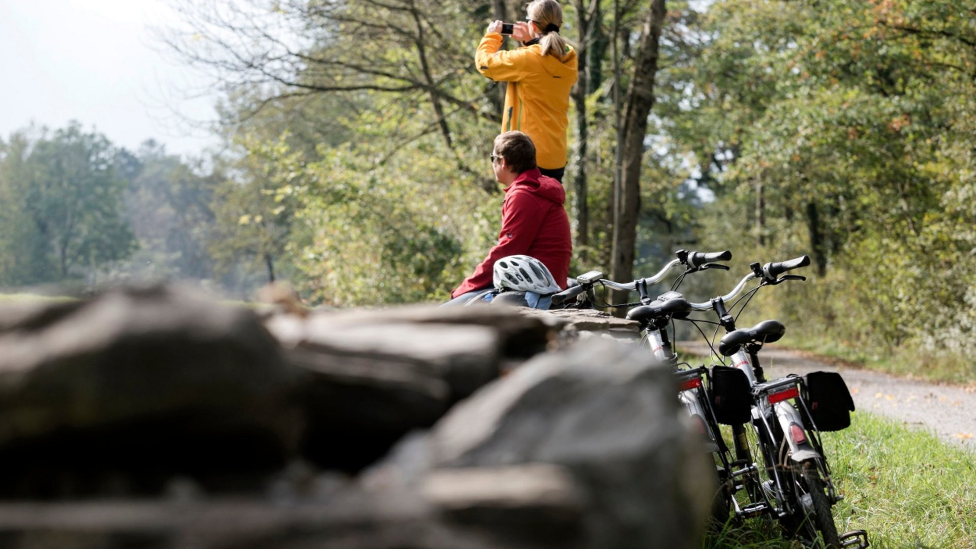 Two cyclists taking a break in the forest, one woman taking a photo