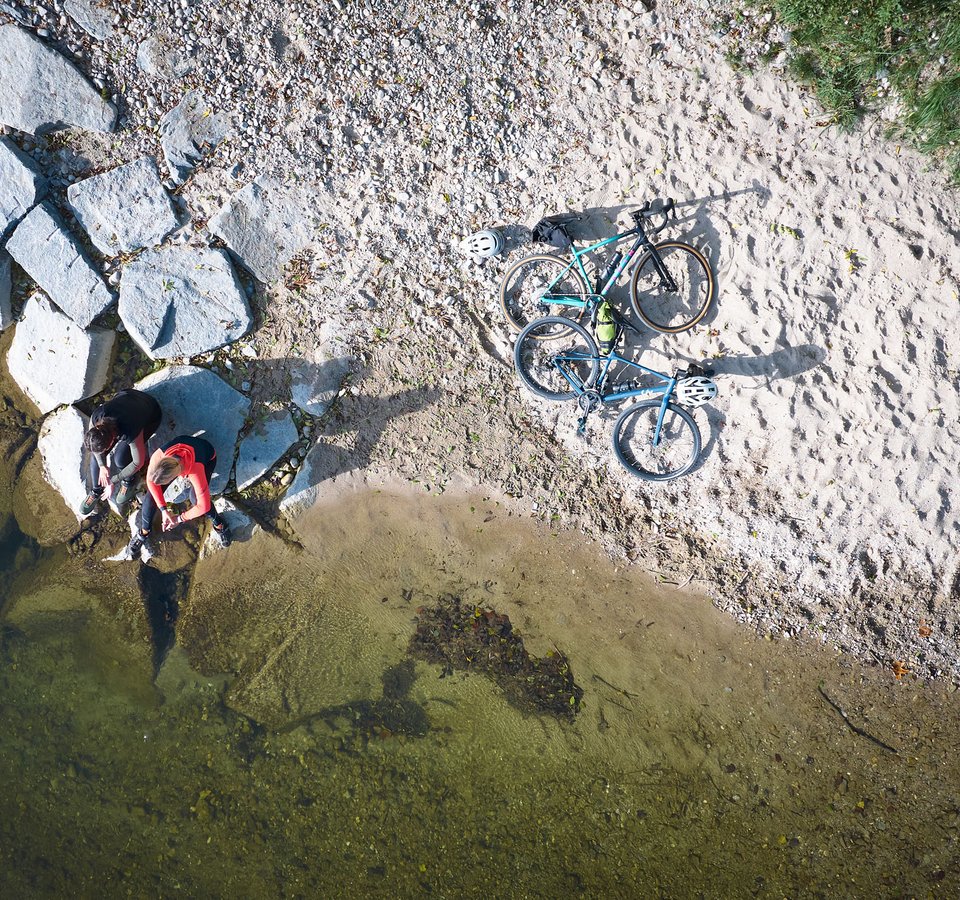 Zwei Personen sitzen am Ufer mit zwei Fahrrädern auf Sand und Felsen