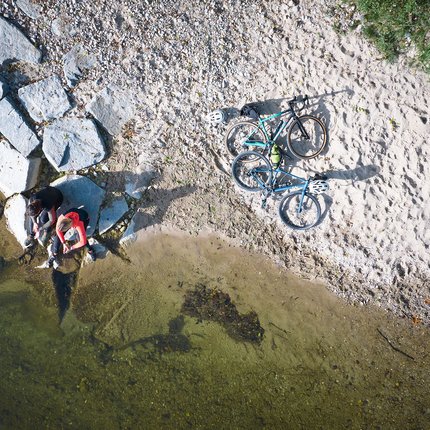 Zwei Personen sitzen am Ufer mit zwei Fahrrädern auf Sand und Felsen
