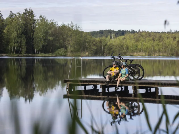 7 Quellen der Entschleunigung © Velontour - Heiko Mandl Zwei Radfahrer sitzen auf einem Steg neben Fahrrädern an einem ruhigen See
