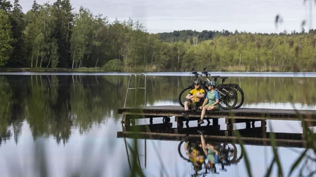 7 Quellen der Entschleunigung © Velontour - Heiko Mandl Zwei Radfahrer sitzen auf einem Steg neben Fahrrädern an einem ruhigen See