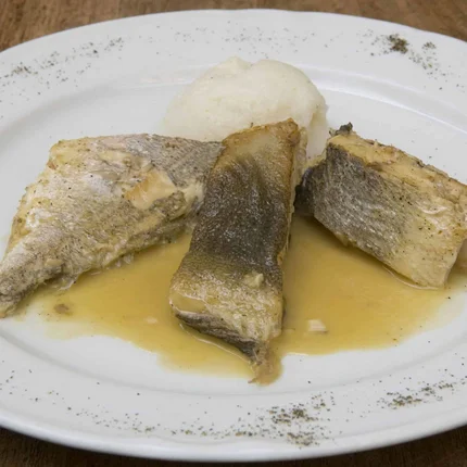 Drie stukken gekookte vis op wit bord met saus en bijgerecht