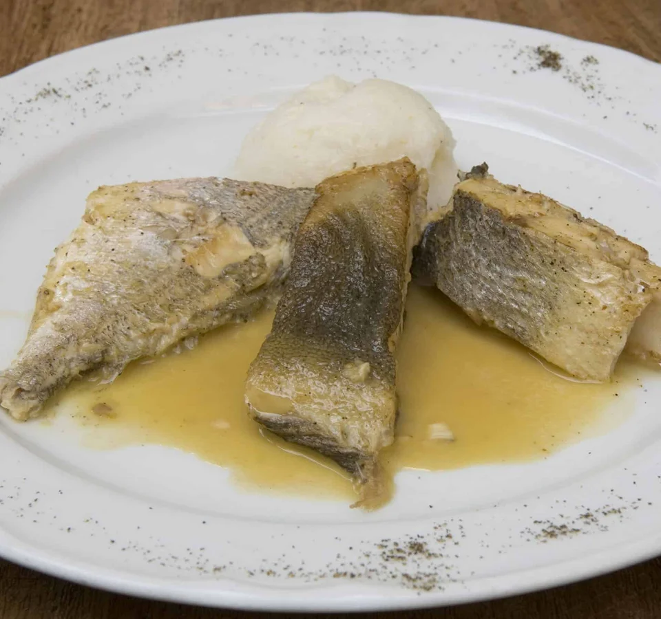 Drie stukken gekookte vis op wit bord met saus en bijgerecht