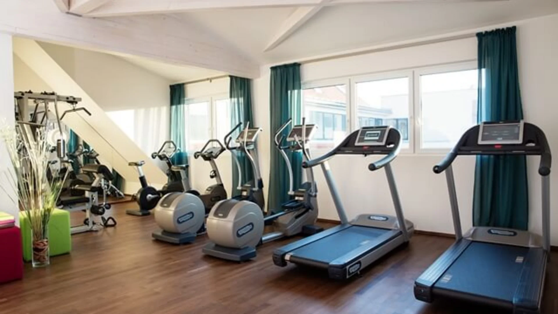 Sportschool met loopbanden en fitnessapparaten bij ramen met blauwe gordijnen