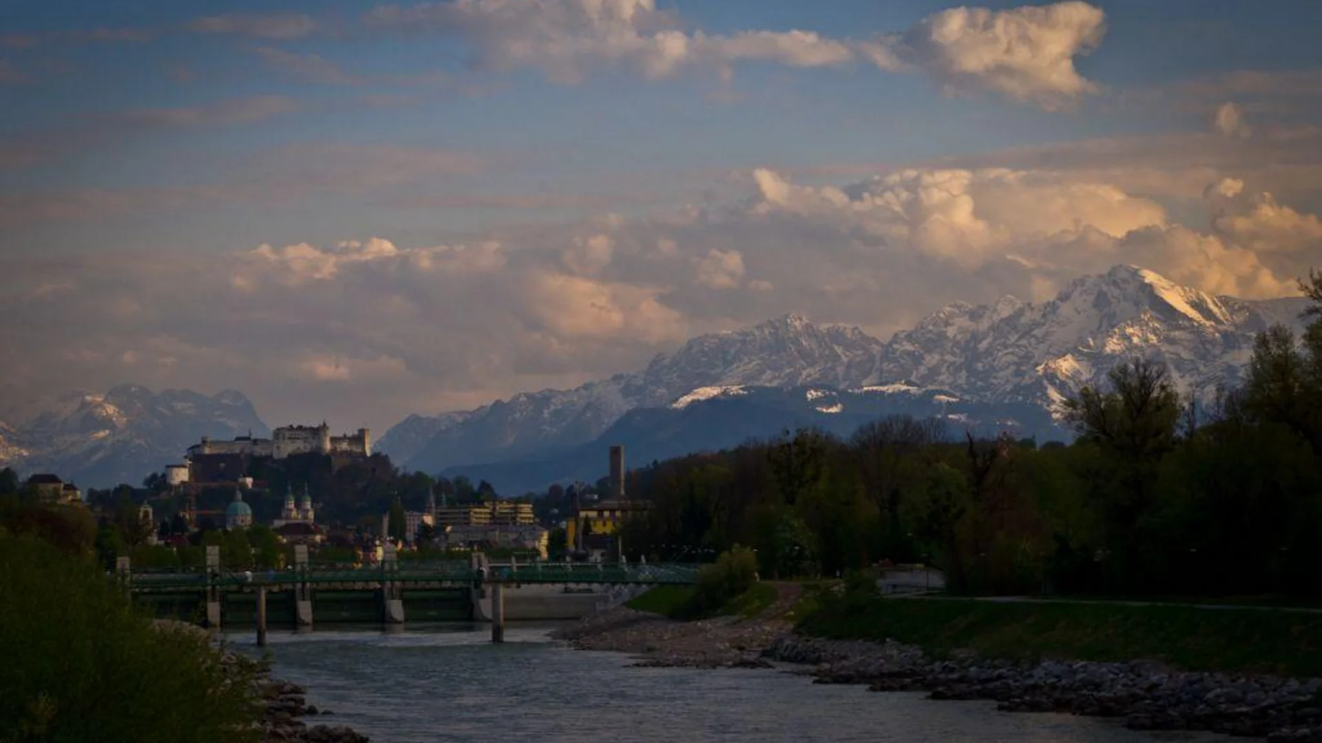 Tour-Detail © Gerald Fimberger Fluss mit Brücke, Stadt im Hintergrund und schneebedeckte Berge bei Sonnenuntergang