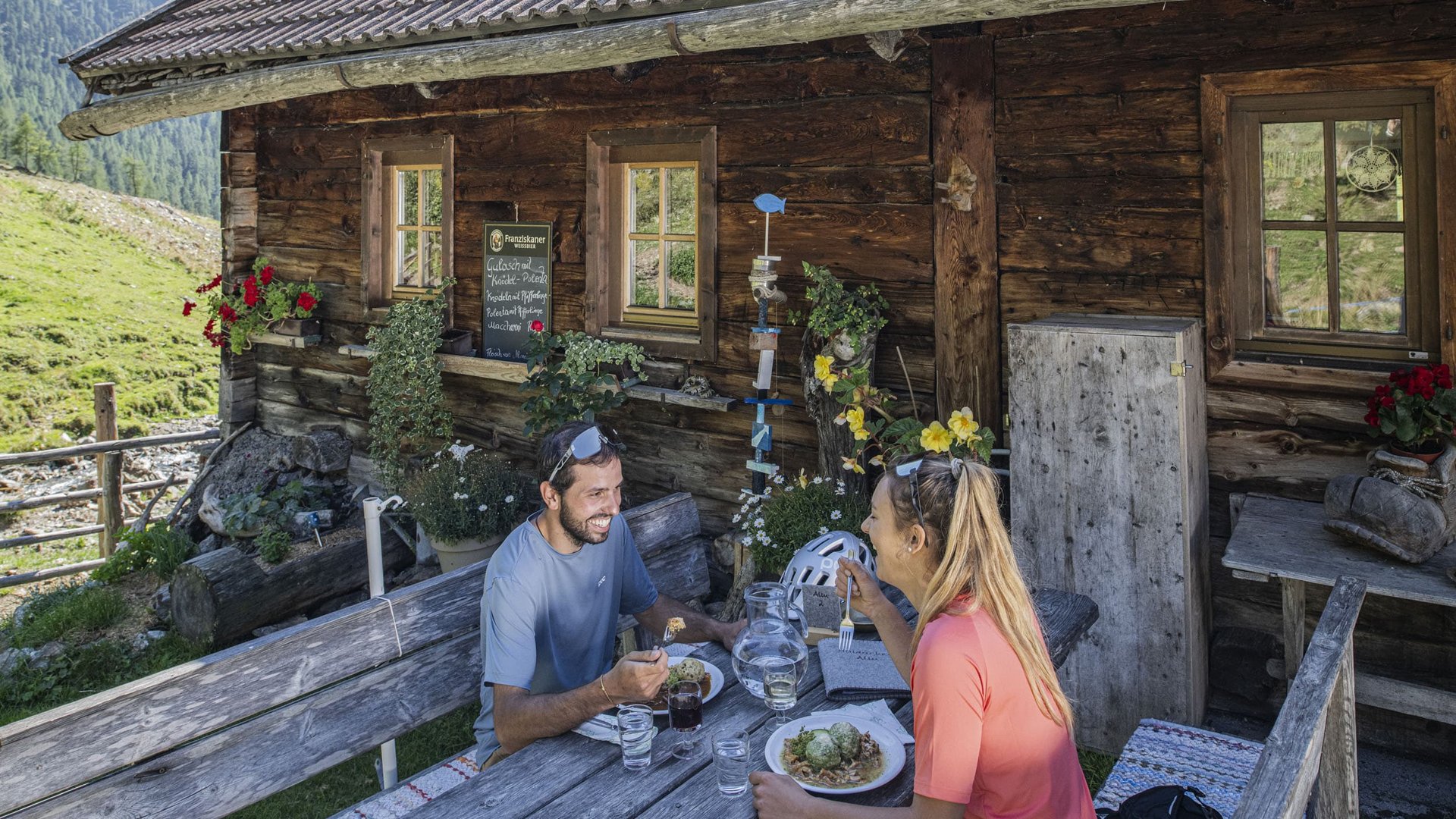 Couple eating outdoors at wooden table in front of mountain hut in the Alps