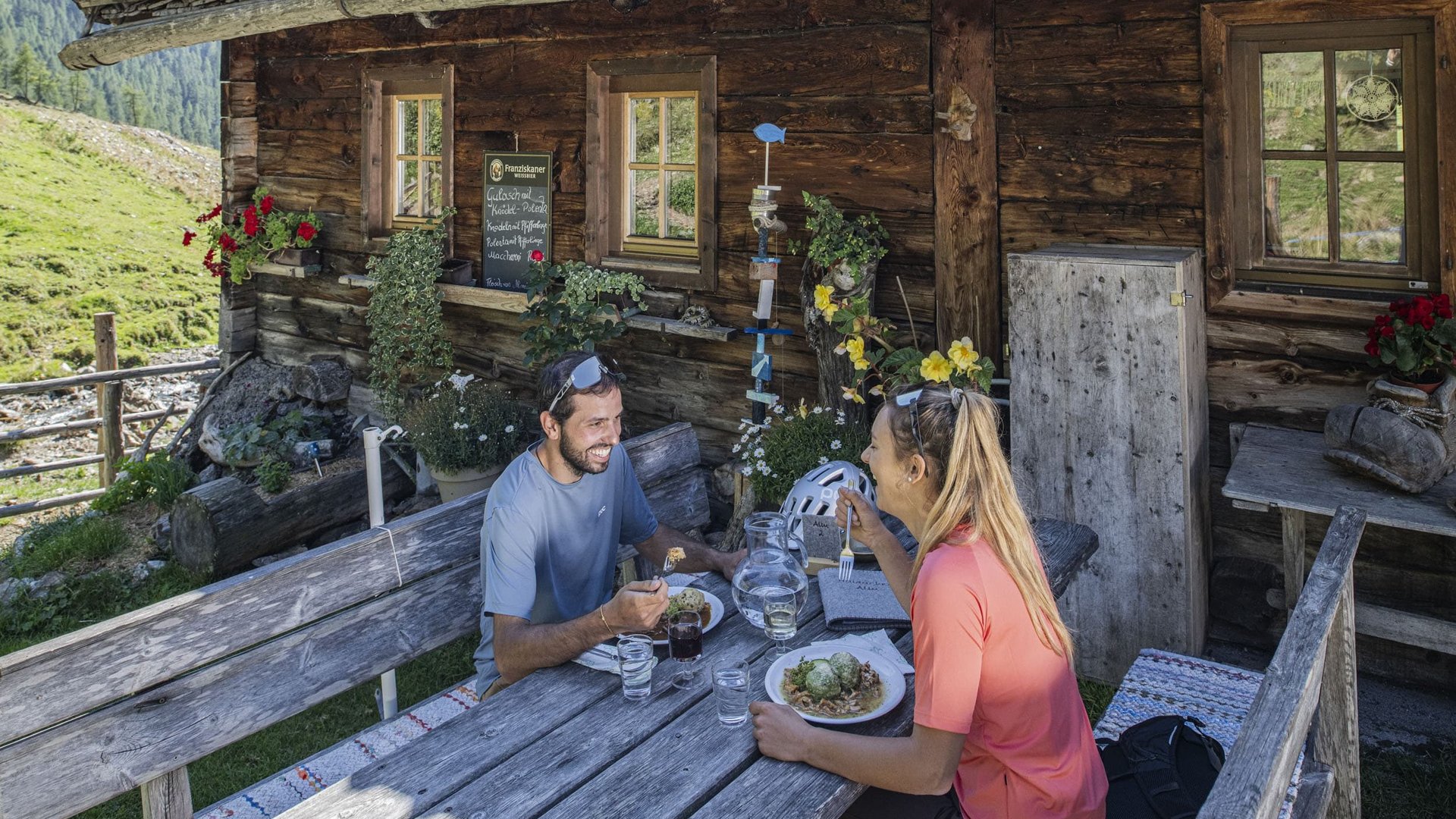 Couple eating outdoors at wooden table in front of mountain hut in the Alps