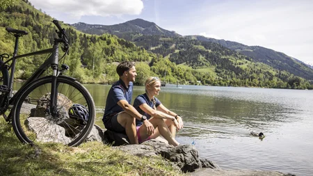 Paar sitzt am Seeufer mit Fahrrad und Blick auf Berge