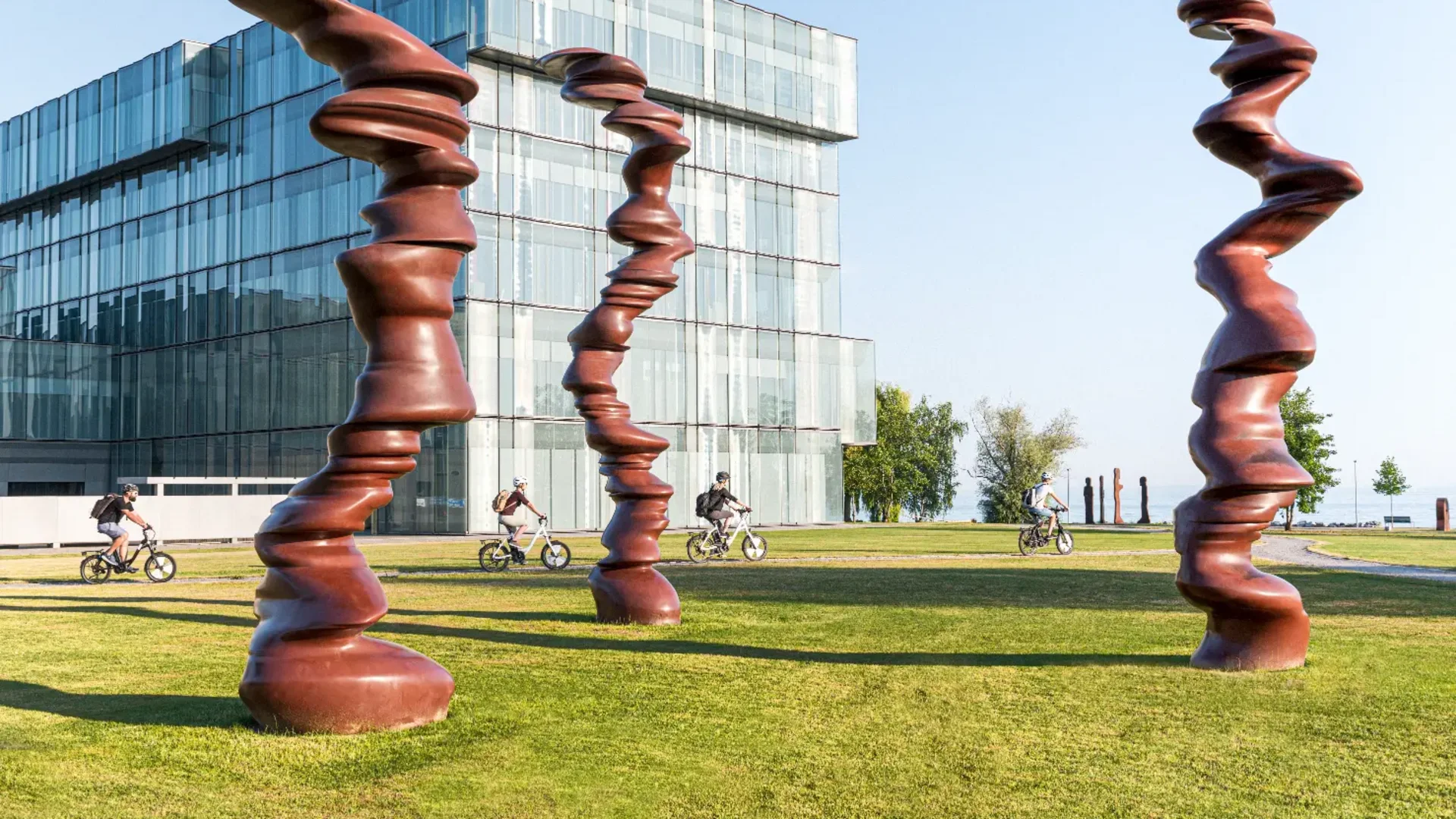 Moderne beeldhouwwerken en fietsers voor glazen gebouw op groen gras