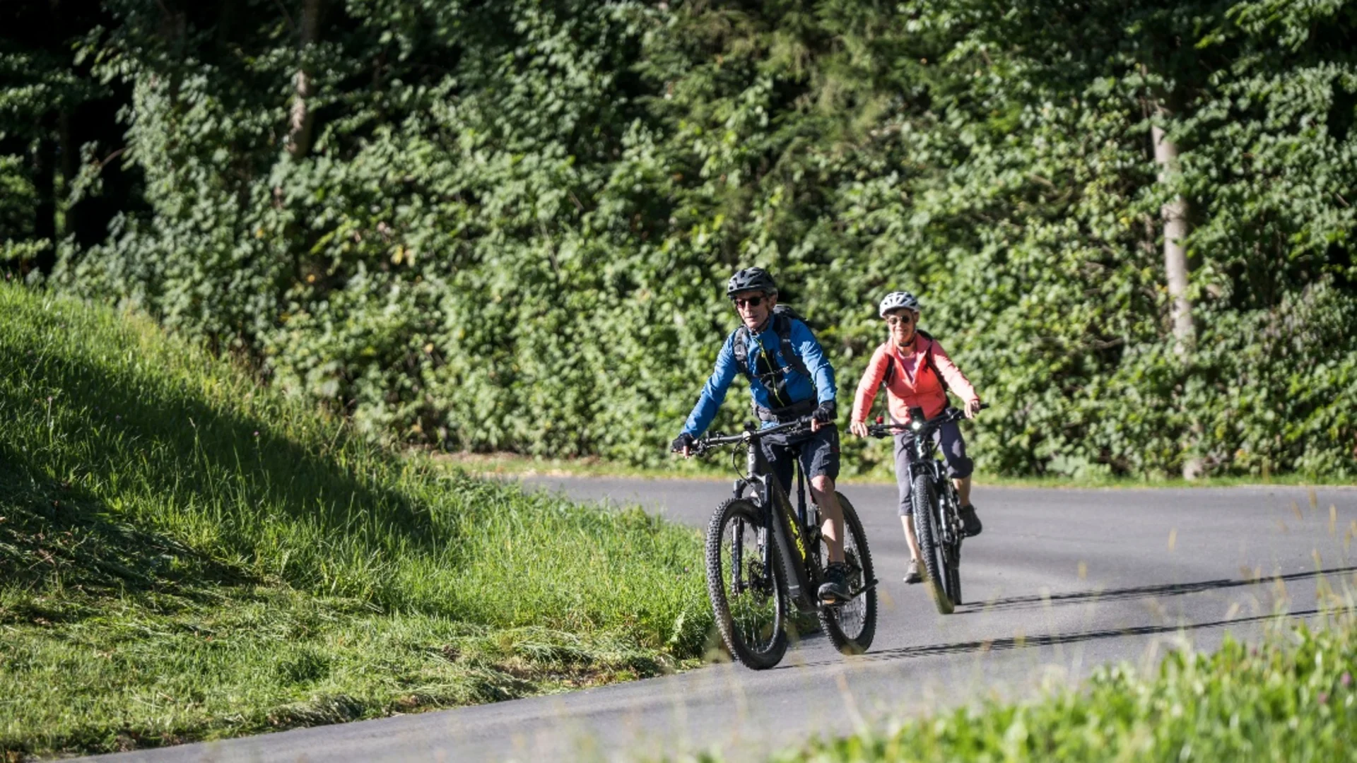 Zwei Radfahrer fahren auf einem Landweg neben grünen Bäumen