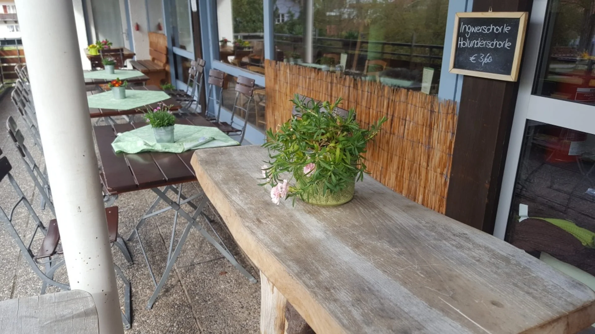 Außenterrasse mit Holztischen, Stühlen und Blumen in Gläsern