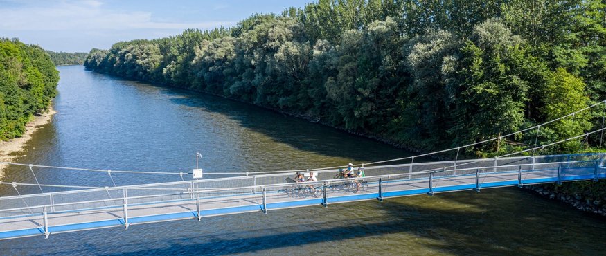 Cyclists crossing a blue suspension bridge over a river